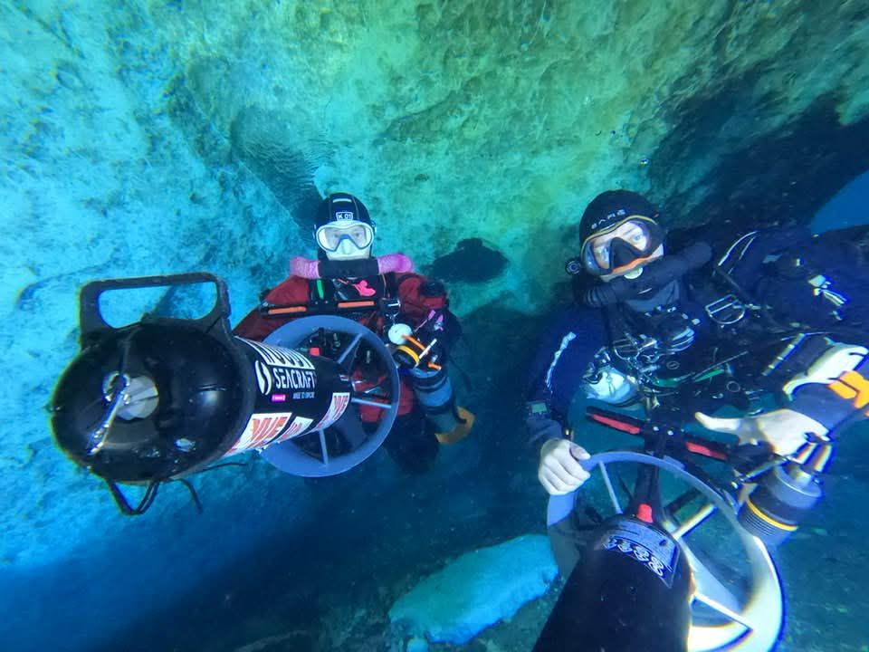 Two cave divers on Seacraft scooters (DPVs) in a blue spring cave